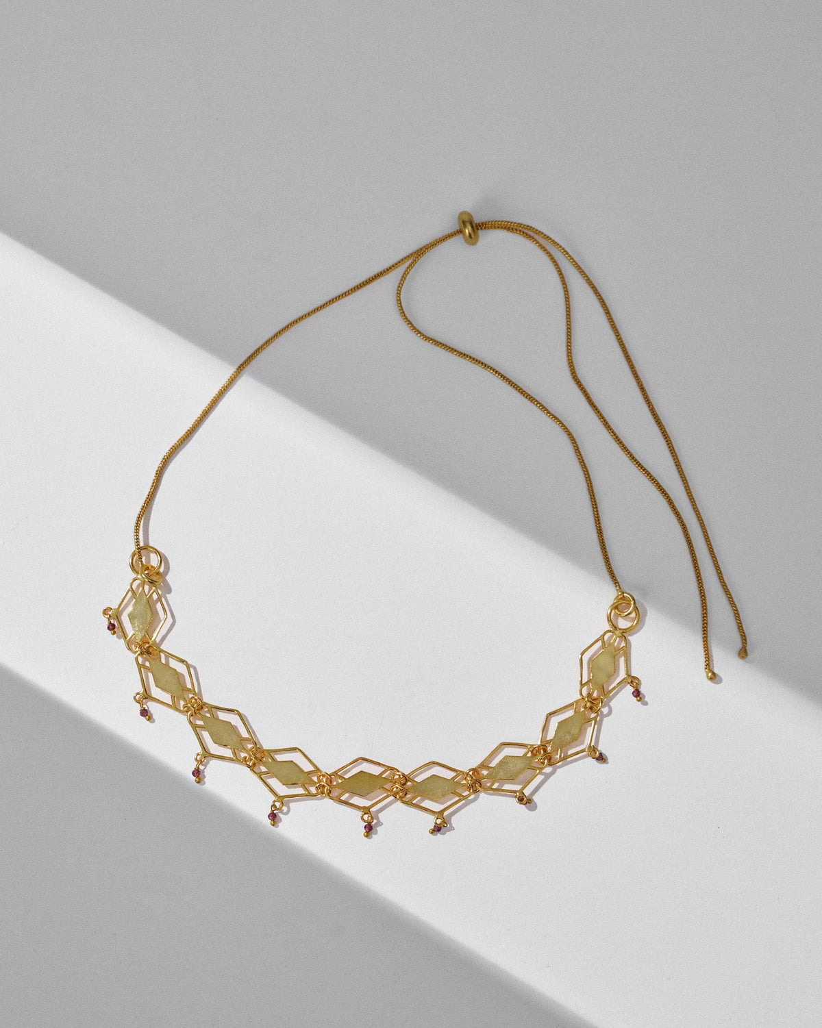 Gold barfi diamond-link necklace with garnet drops and an adjustable chain.