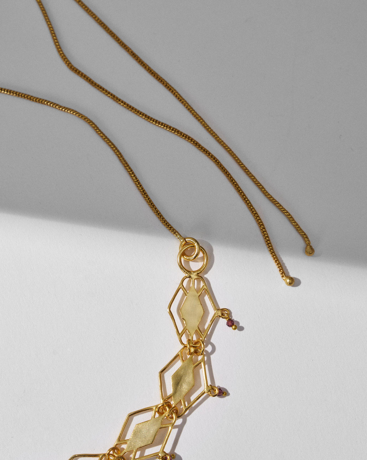 Close-up of gold diamond-shaped links with small red garnet drops.