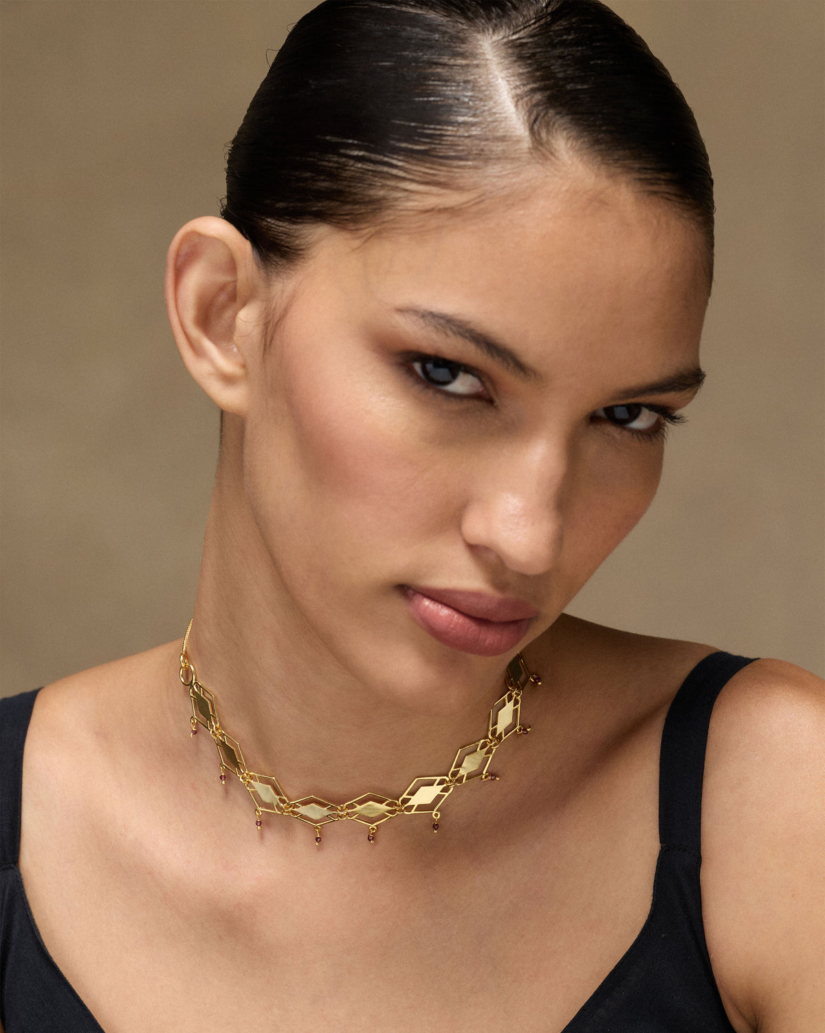 Person wearing a gold diamond-link choker with hanging red garnet drops.
