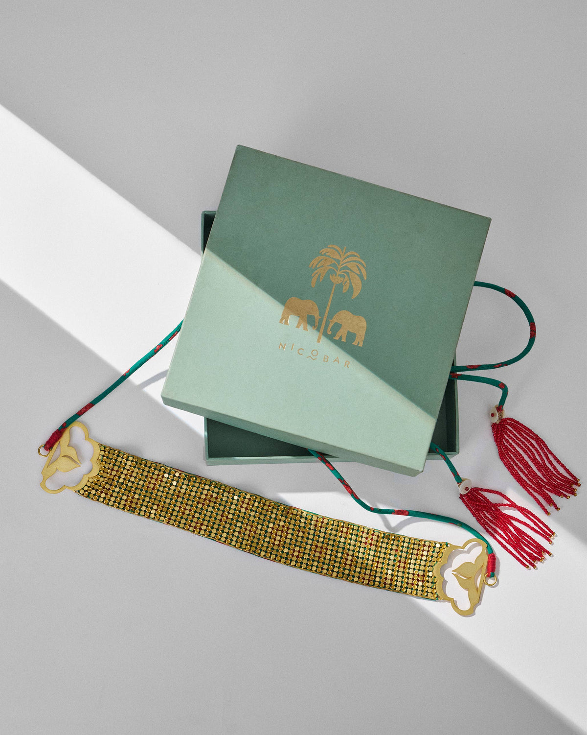 Gold Chain Mail necklace with red tassels and a sage Nicobar gift box.