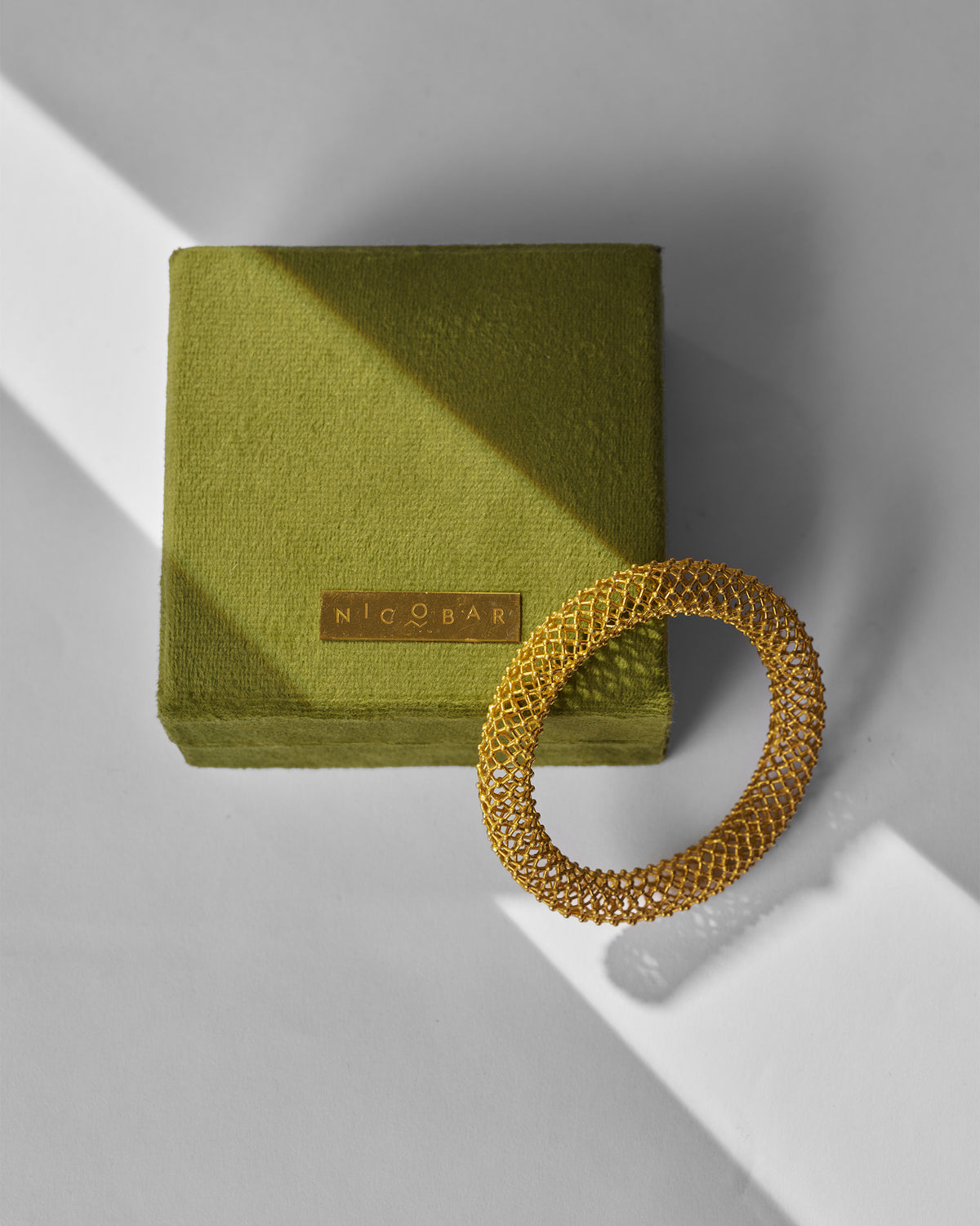 Gold mesh Infinity bangle beside an olive Nicobar jewellery box.