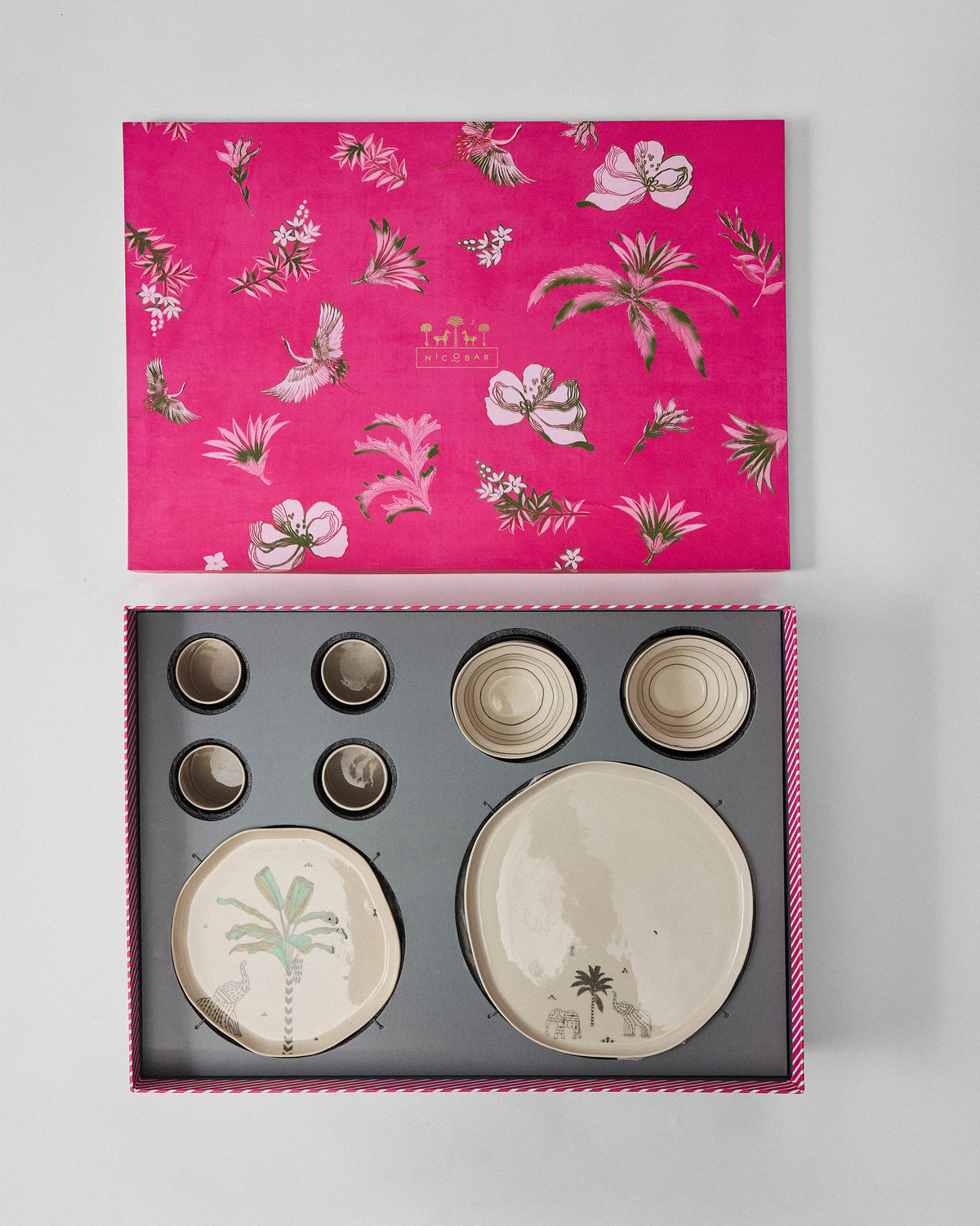 Ceylon Trail Dinner Gift Set in its open pink box, with palm-print plates and bowls.