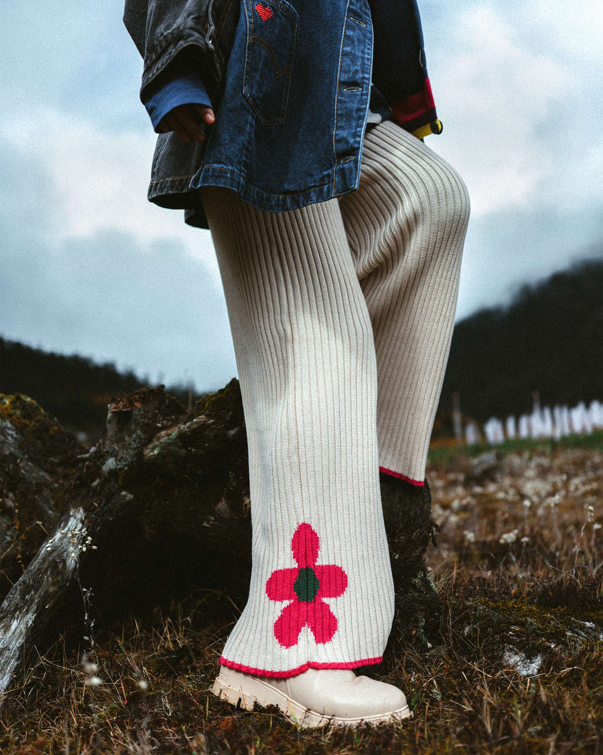 Person wearing ivory rib knit trousers with a pink flower at the hem.