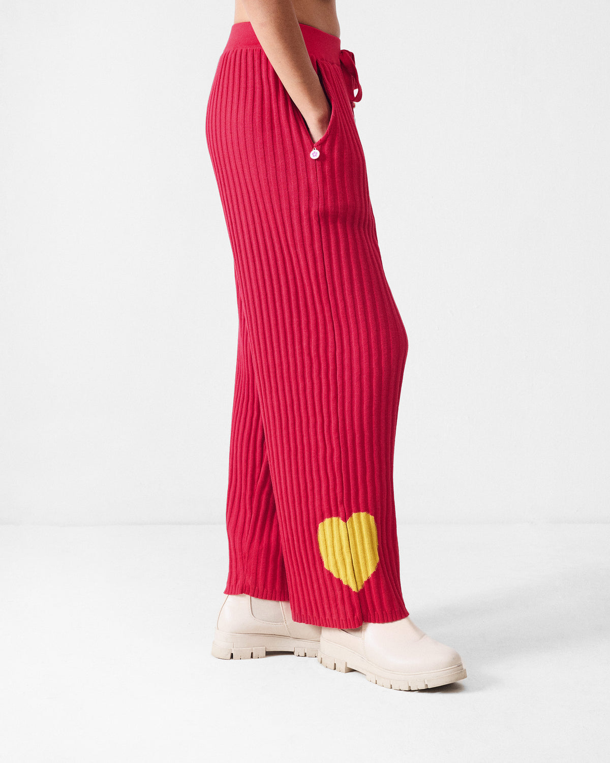 Side view of red rib-knit pants with a yellow heart and side pocket.