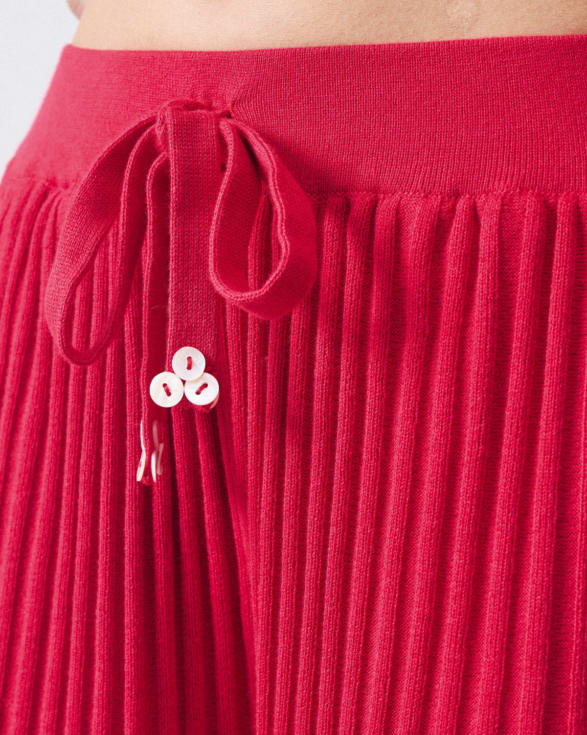 Close-up of red rib-knit pants with a drawstring and white flower buttons.