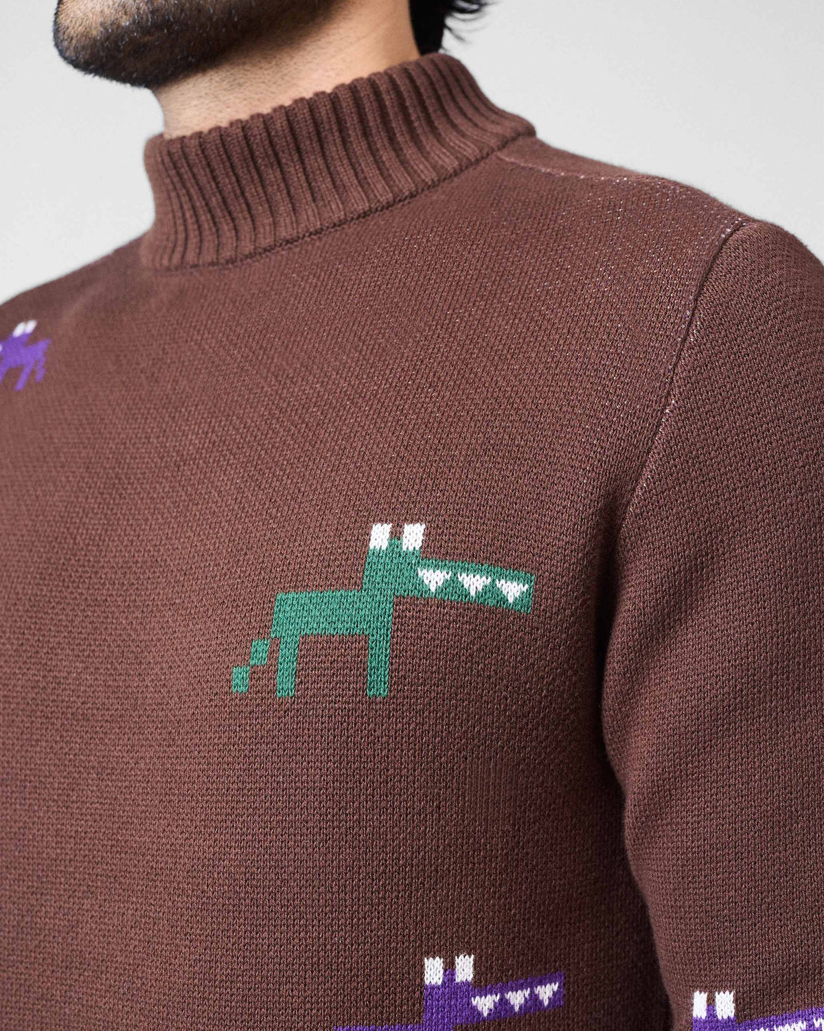 Close-up of a green pixel animal motif on a brown crew neck sweater.