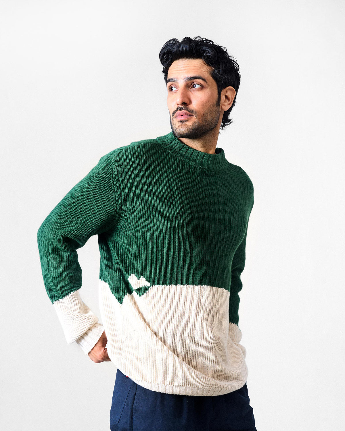 Three-quarter view of a green and ivory crew neck sweater with a heart motif.