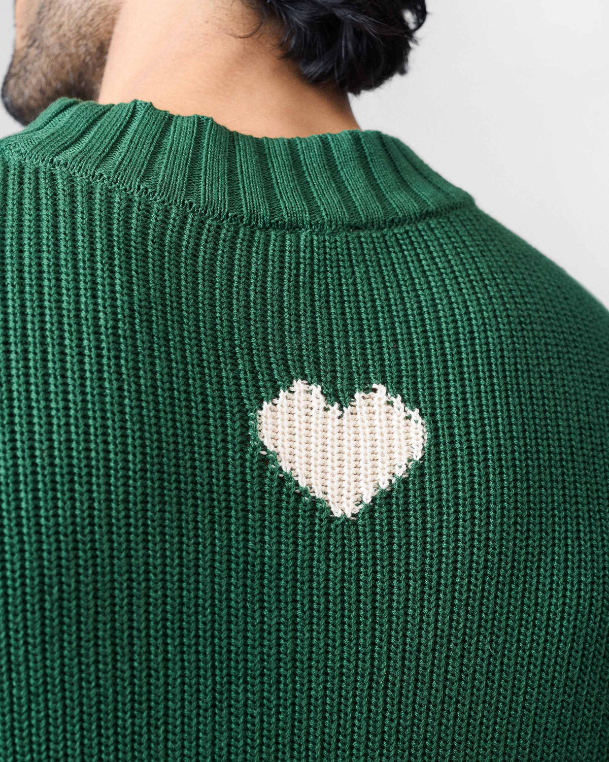 Close-up of a cream heart knitted on the back of a green crew neck sweater.