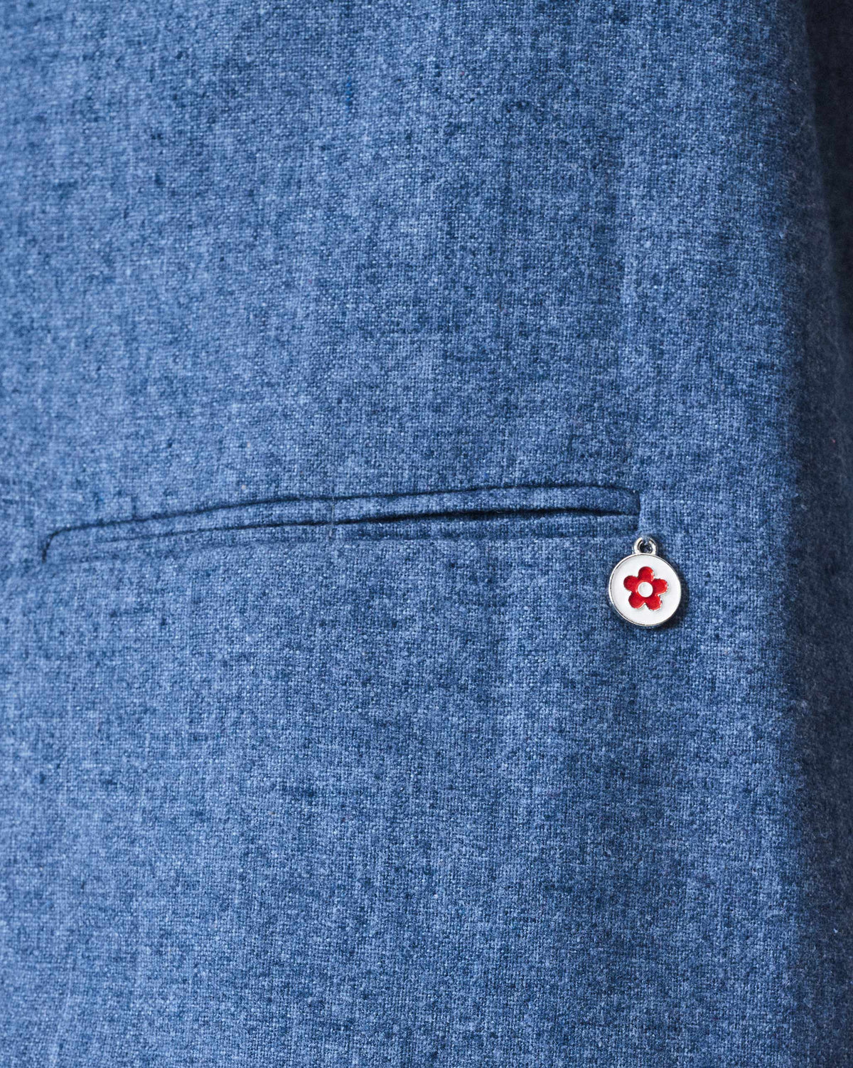 Close-up of a welt pocket and flower charm on a dust blue Trace Jacket.