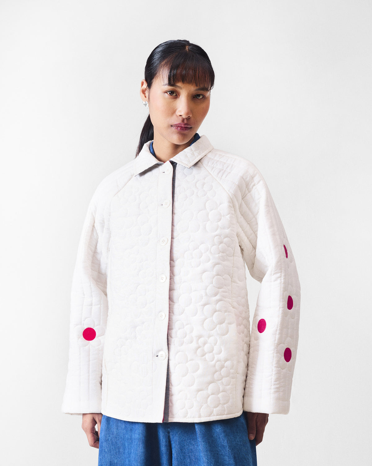 Person wearing an ivory quilted Botanik jacket with fuchsia sleeve flower accents.
