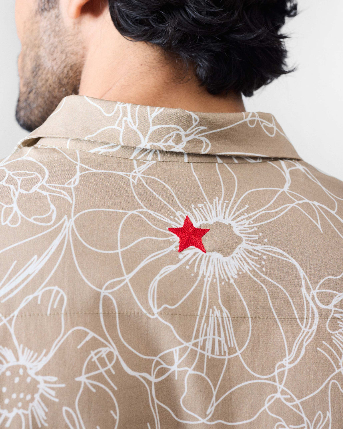 Close-up of a red star on the back of a light brown Hakuna Shirt.