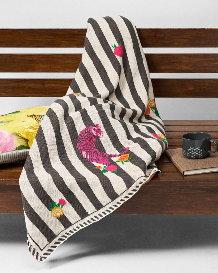 Ara Throw draped over a surface, with a pink tiger and rose sprigs on black and cream stripes.