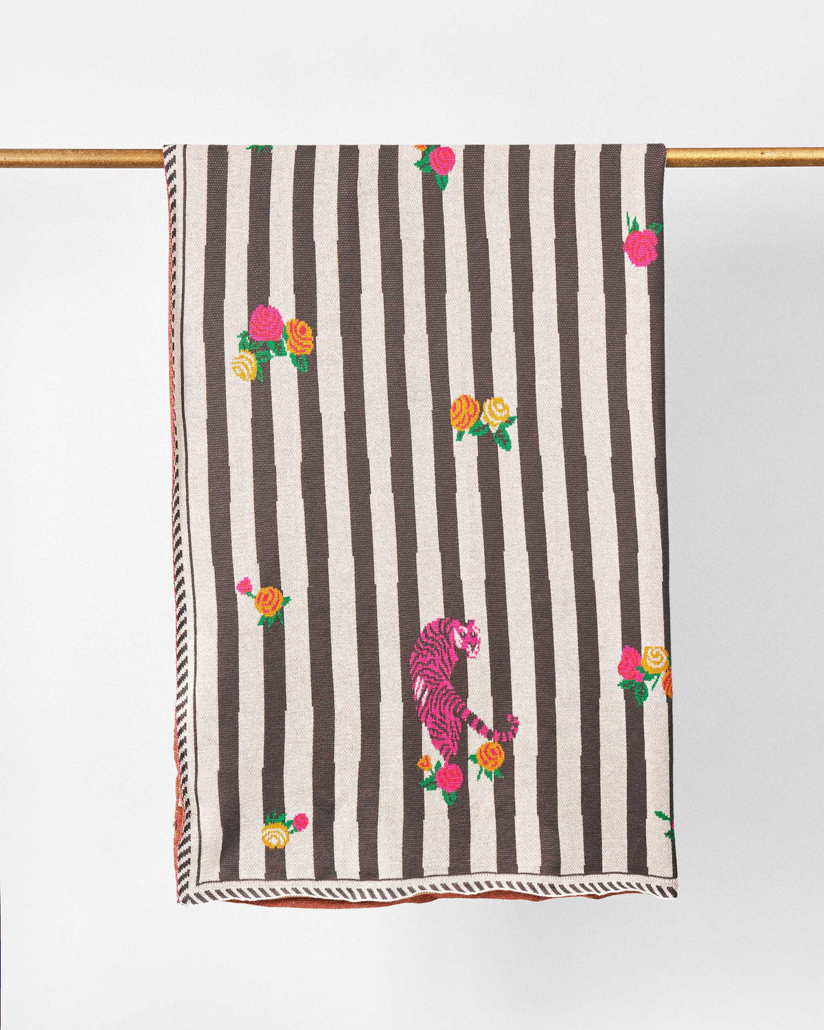 Ara Throw hanging over a gold rail, showing its striped pattern and rose sprigs.