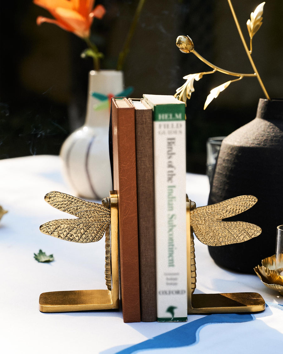 Gold dragonfly bookends holding books on a table with vases