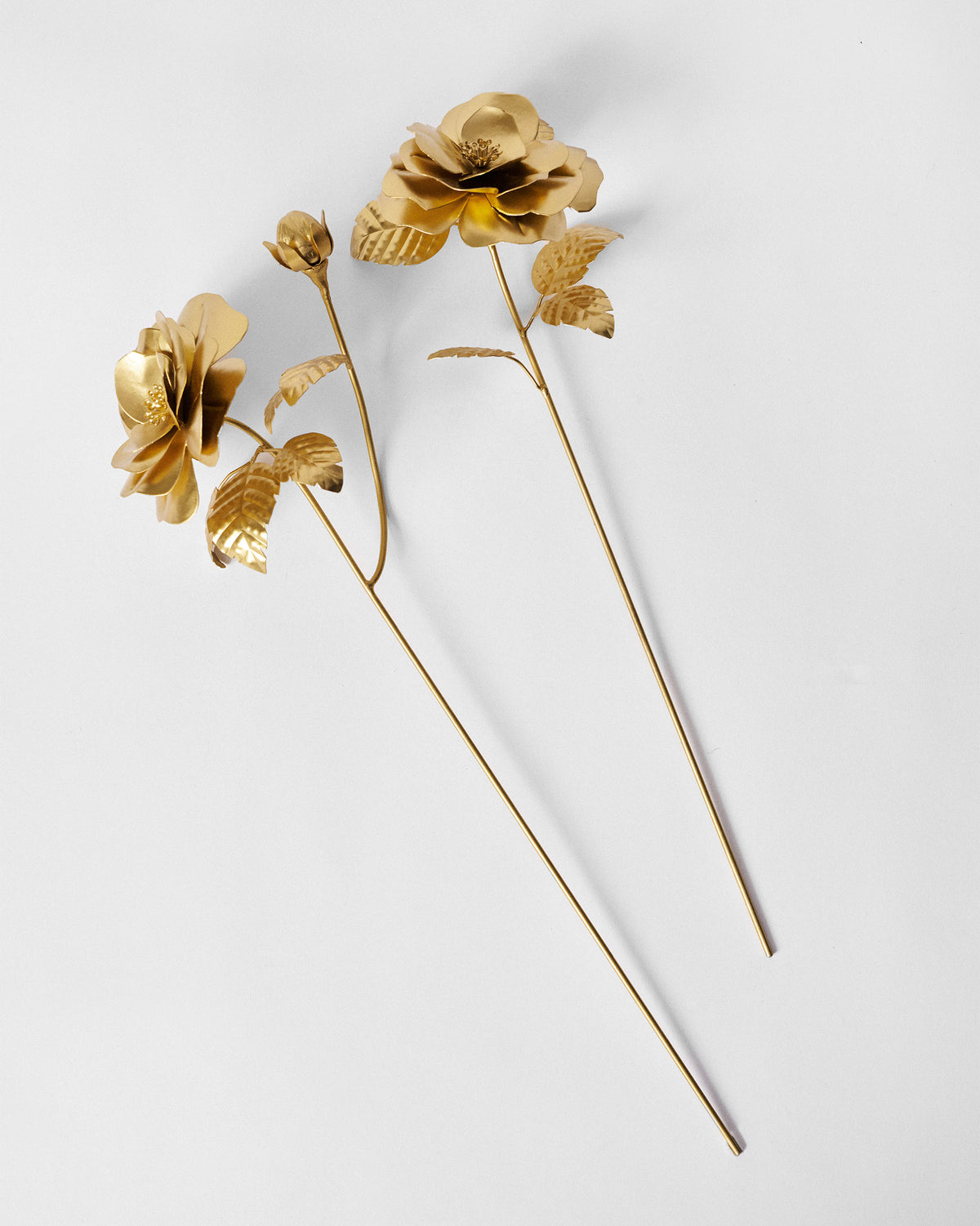Pair of matte gold rose home accents with leaves and a bud laid flat.