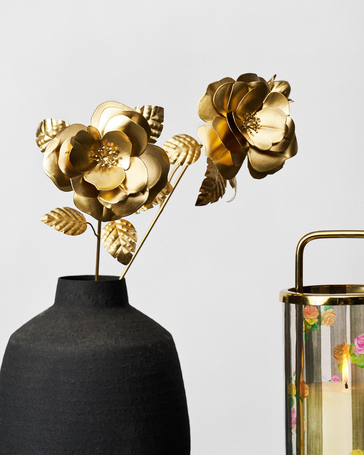 Matte gold rose home accents styled upright in a dark ceramic vase.