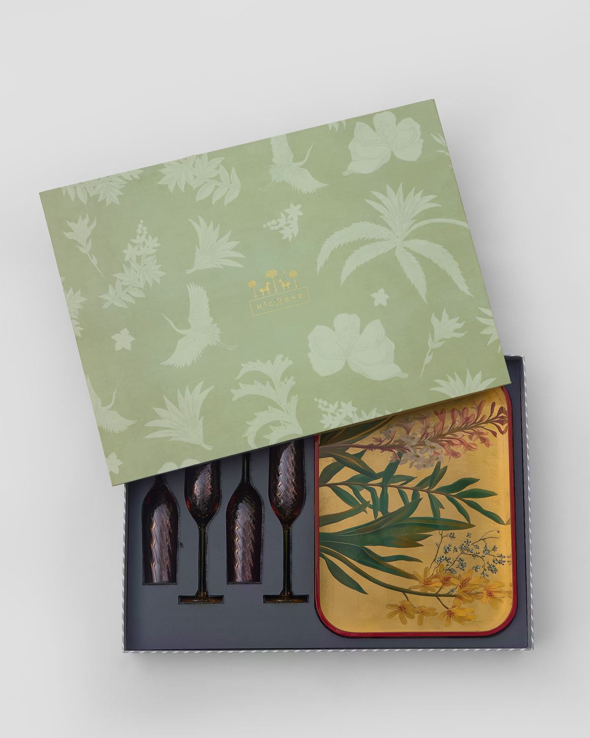 Open gift box with four tinted flutes and a botanical serving tray.