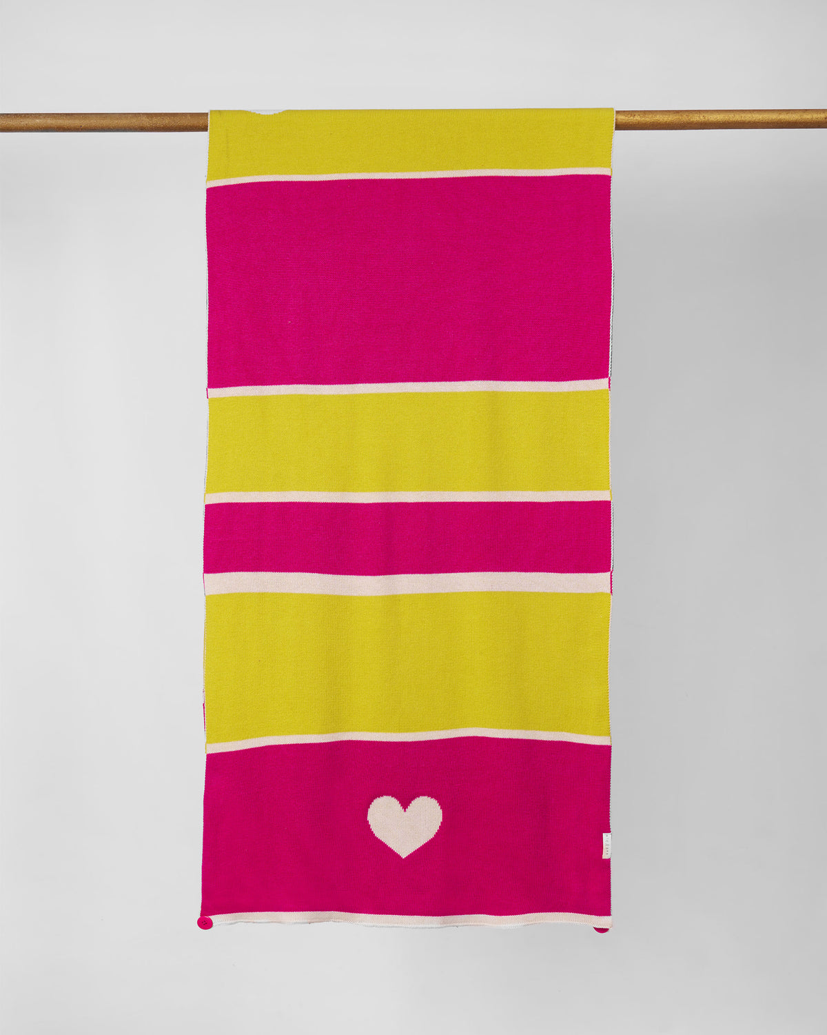 Full Chromatic Crossroads scarf hung from a rod, pink and yellow stripes with a white heart.