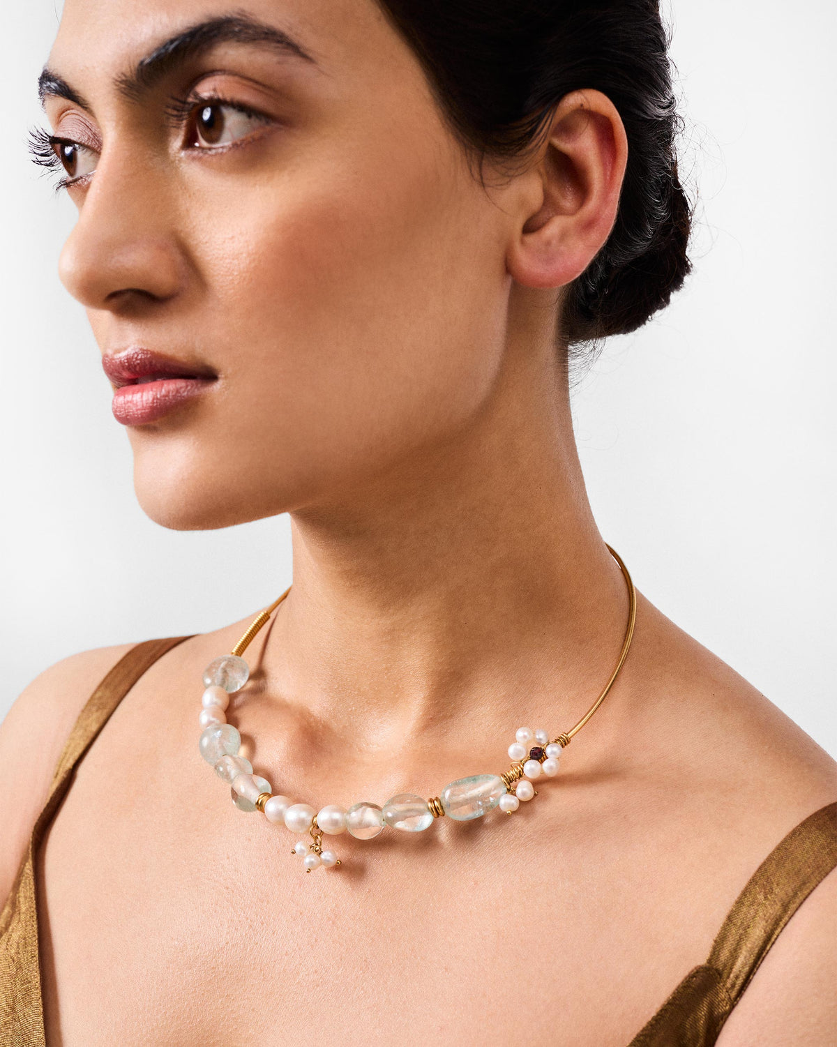 Person wearing a Noorani gold wire collar with pale blue stones and pearls.