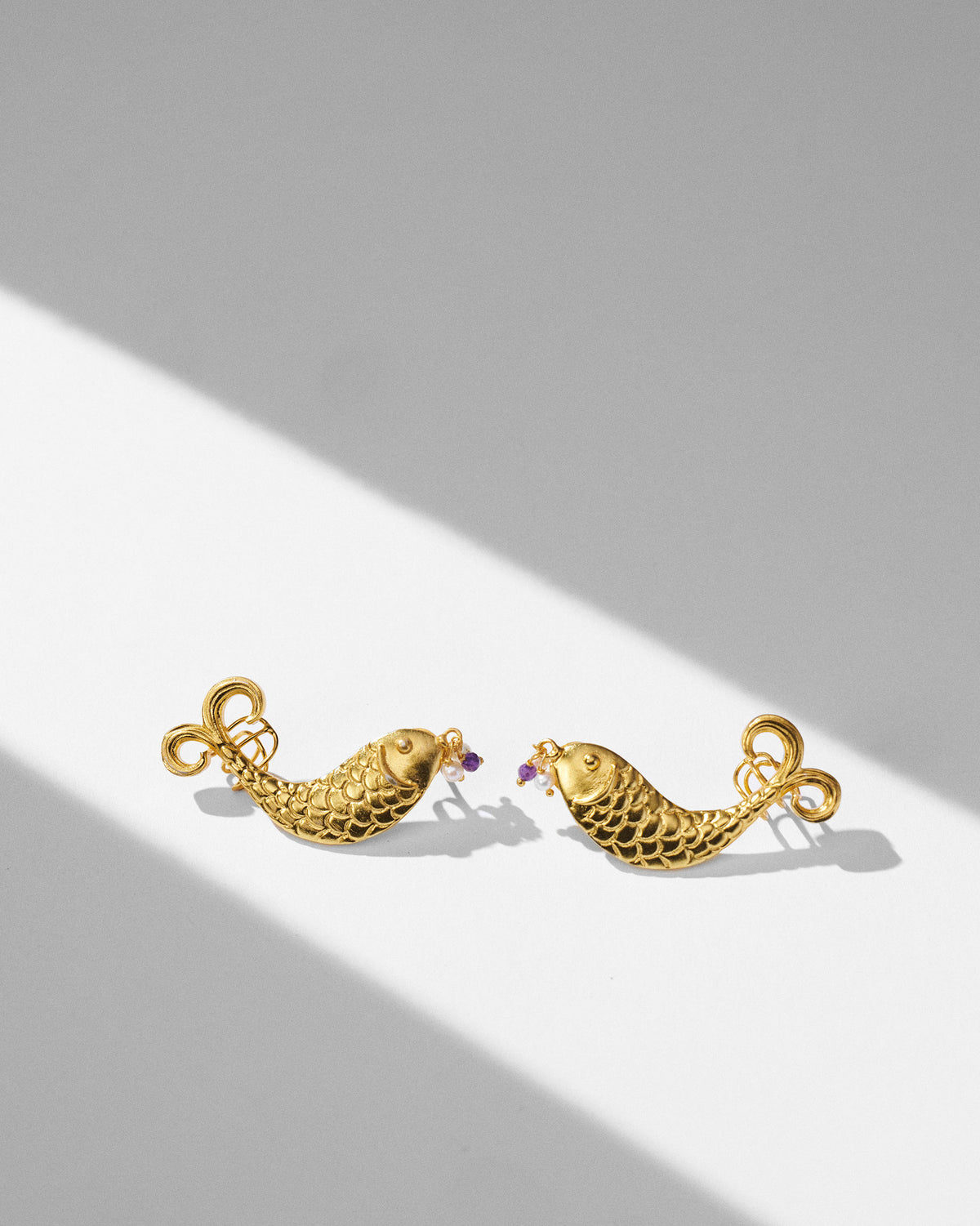 Gold Dupki fish studs facing each other with pearl and purple beads.
