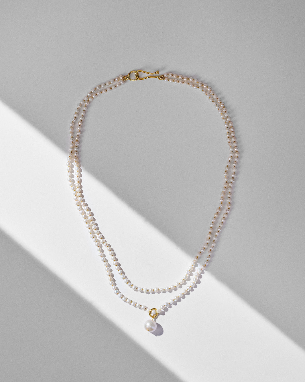 Double-strand Chandni pearl necklace with a single pearl drop laid flat.