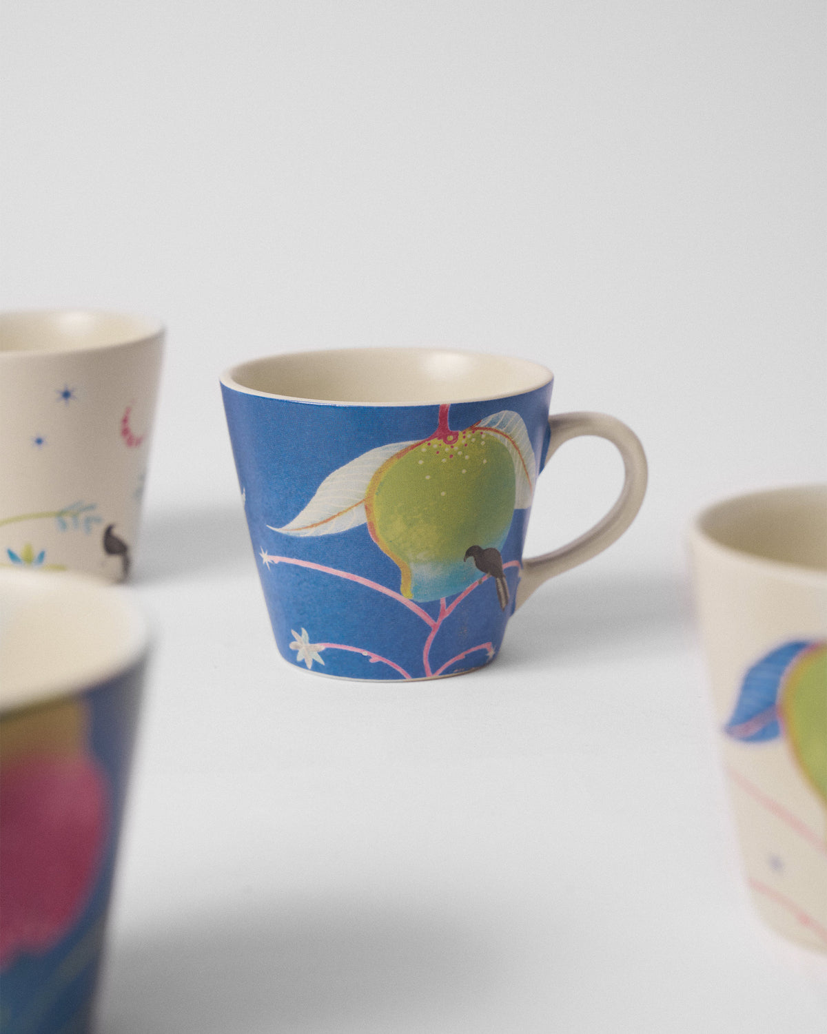 Close-up of a blue Ambi Espresso Mug with a green mango and bird motif.