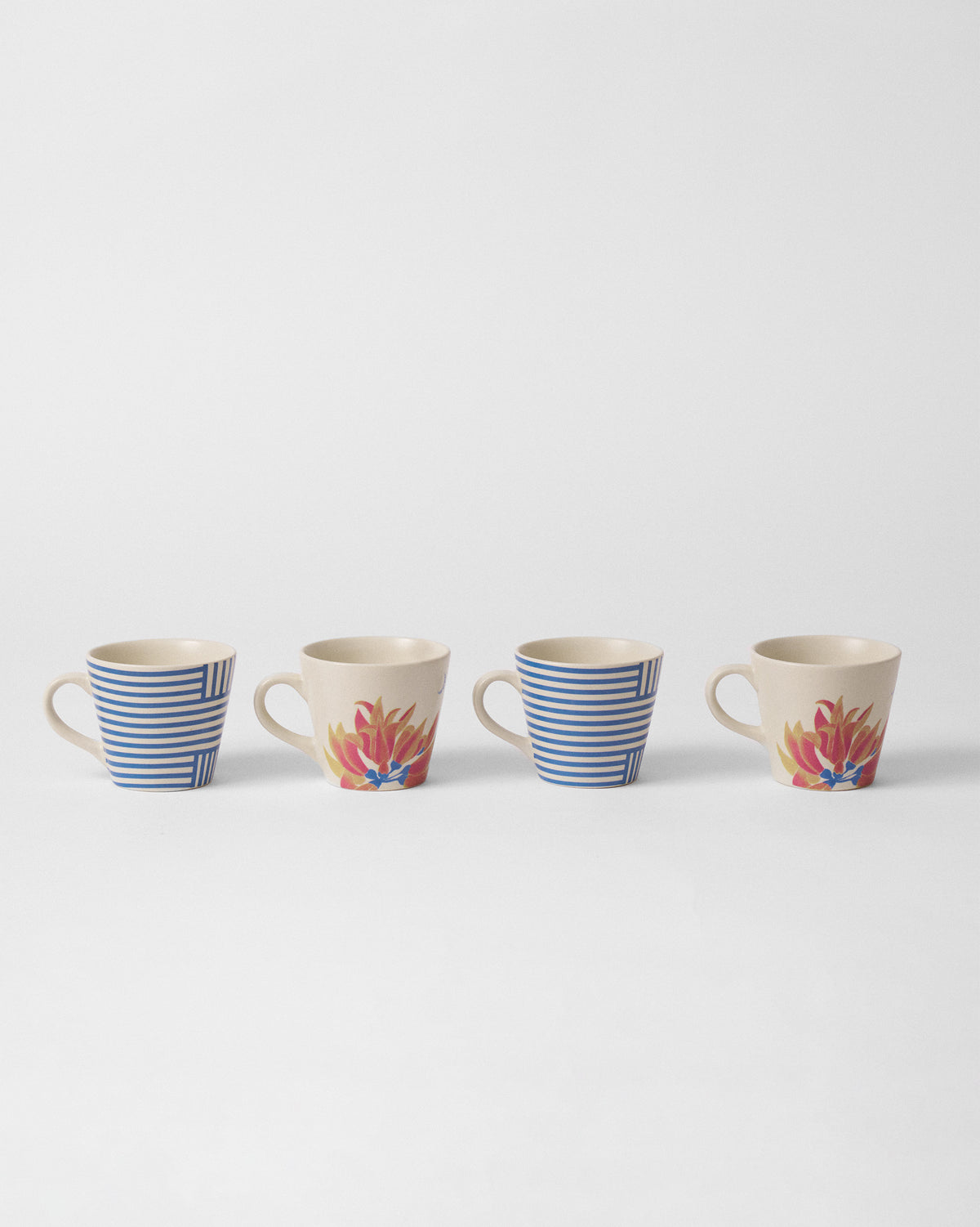Four Koel espresso mugs lined up showing blue stripe and palash flower sides.