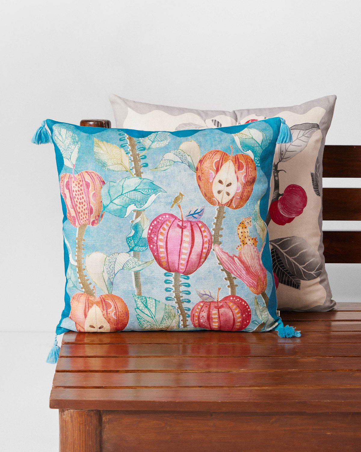 Seb cushion cover in turquoise with pink fruit motifs and blue tassels.