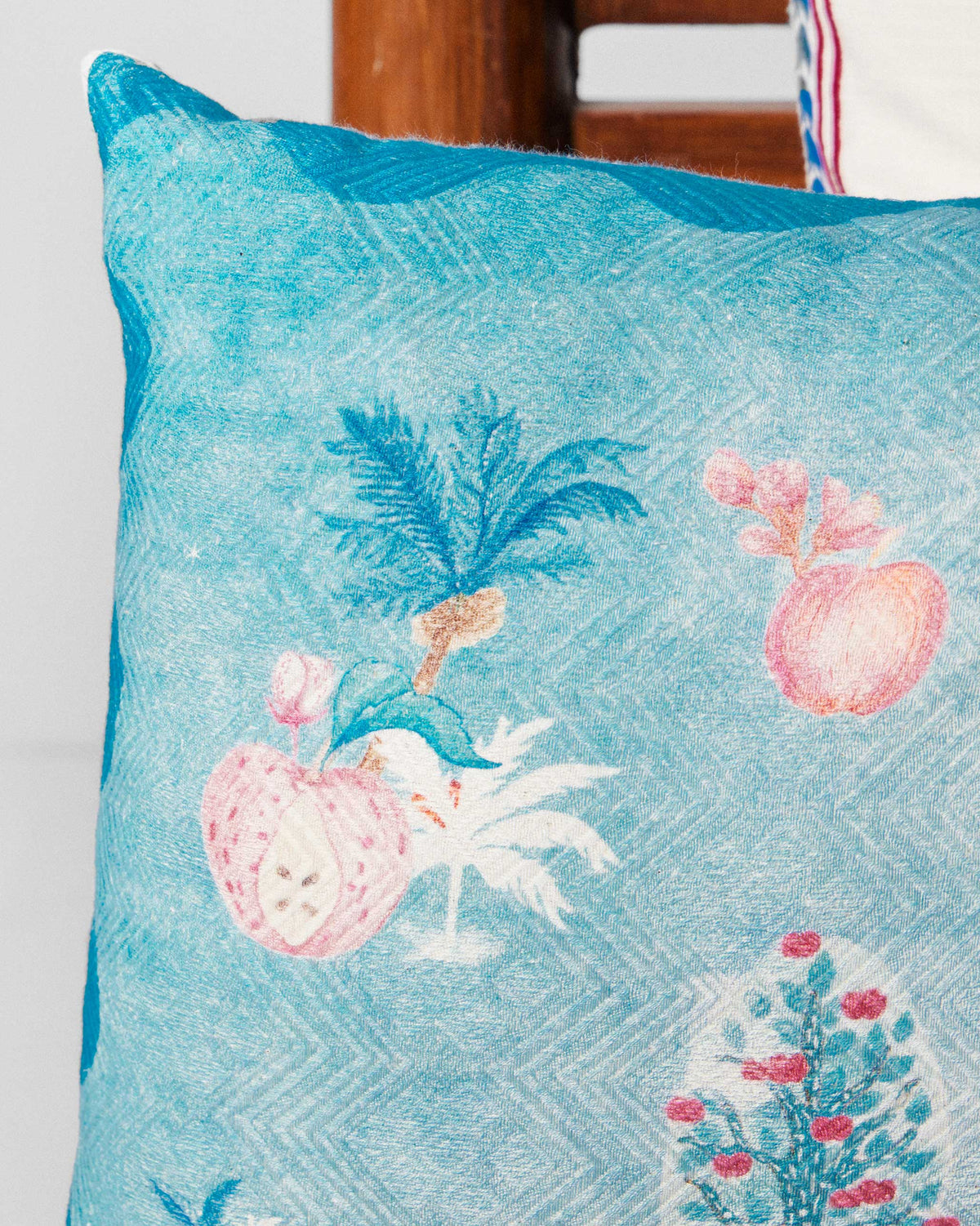 Close-up of Aaranya cushion cover showing pink fruit and tree motifs in teal.
