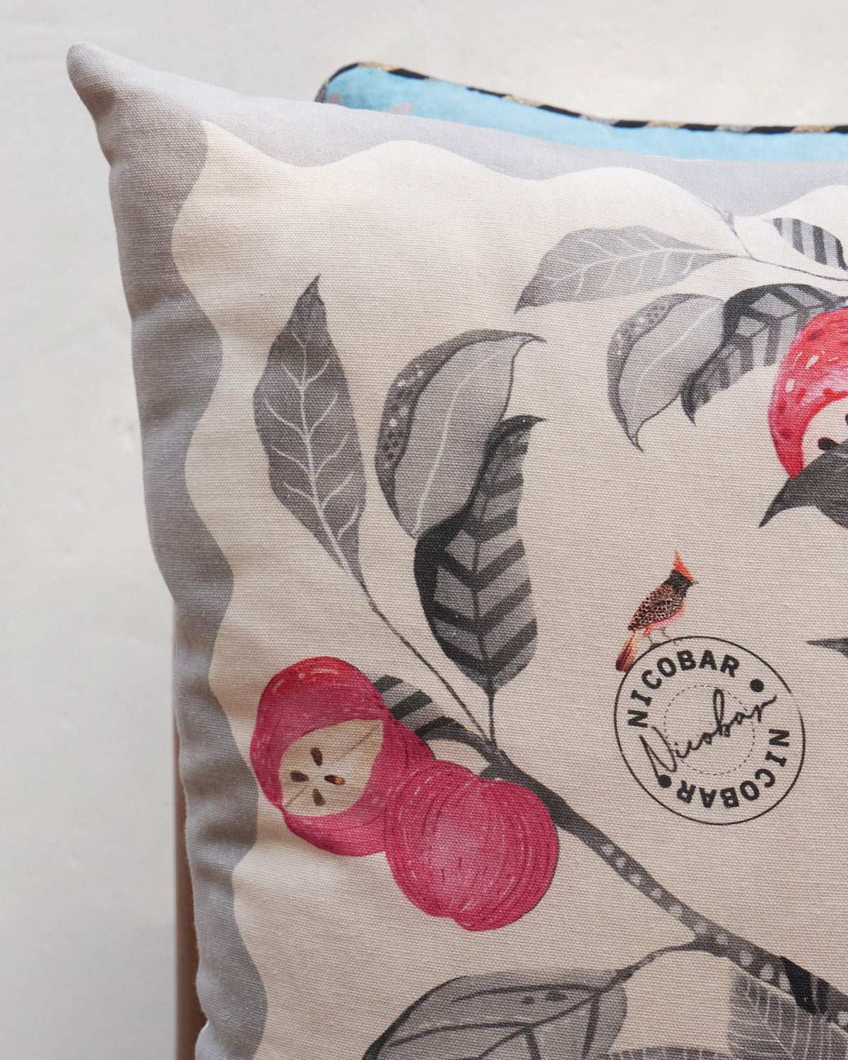Close-up of Orchard cushion cover showing red fruit, leaves and a cardinal bird.