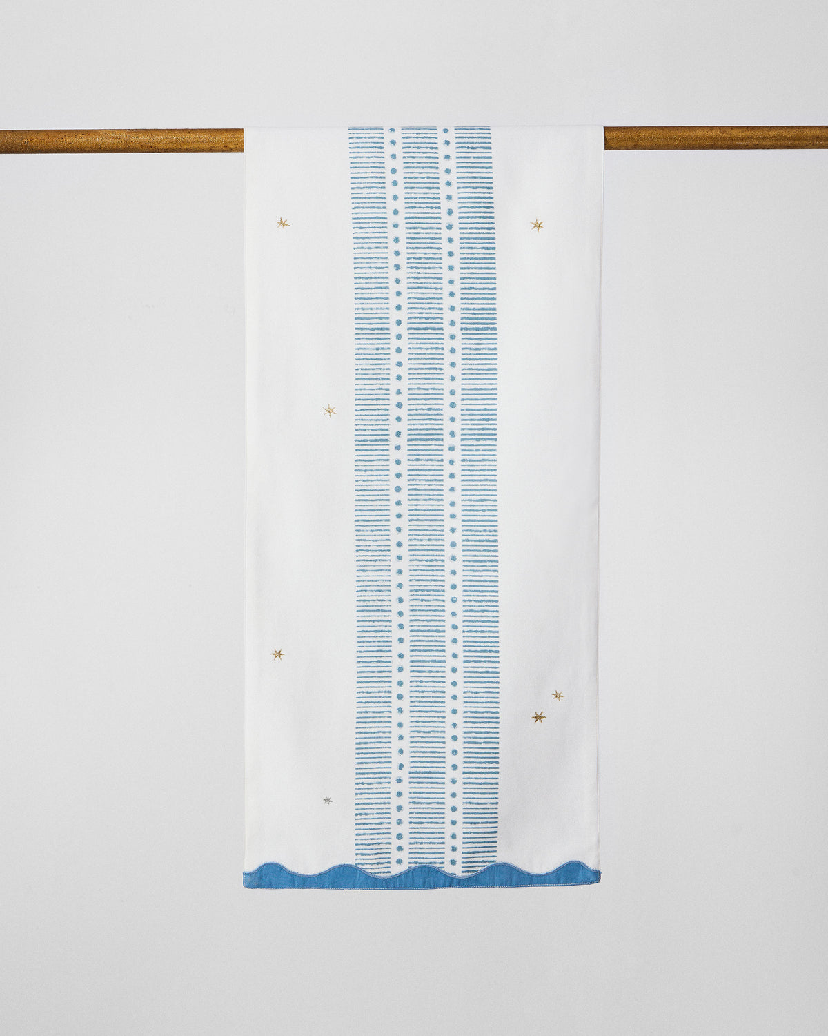 Ambi table runner hanging to show blue stripes, gold stars, and scalloped hem.