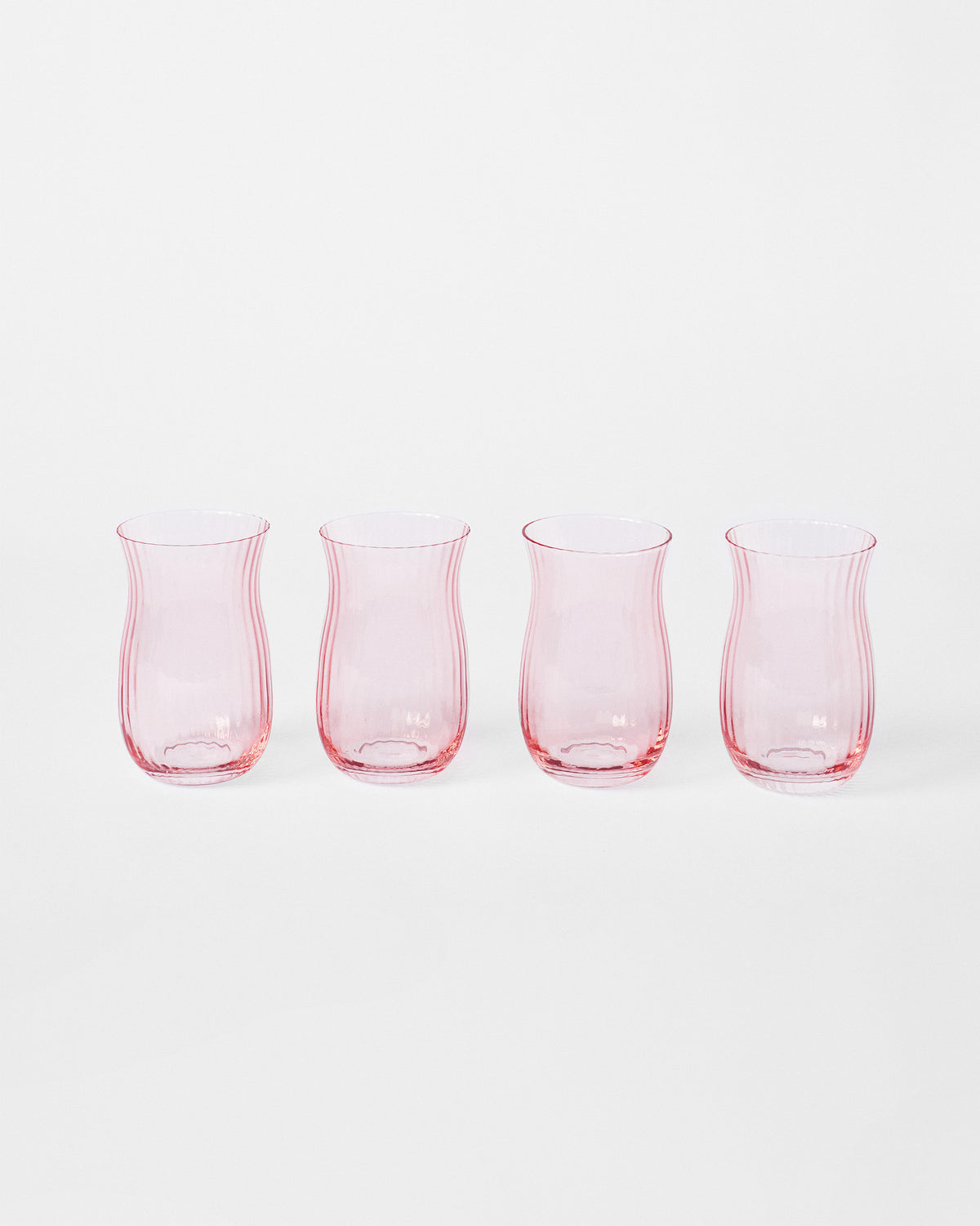 Set of four blush pink Ripple Glass tumblers in a row.