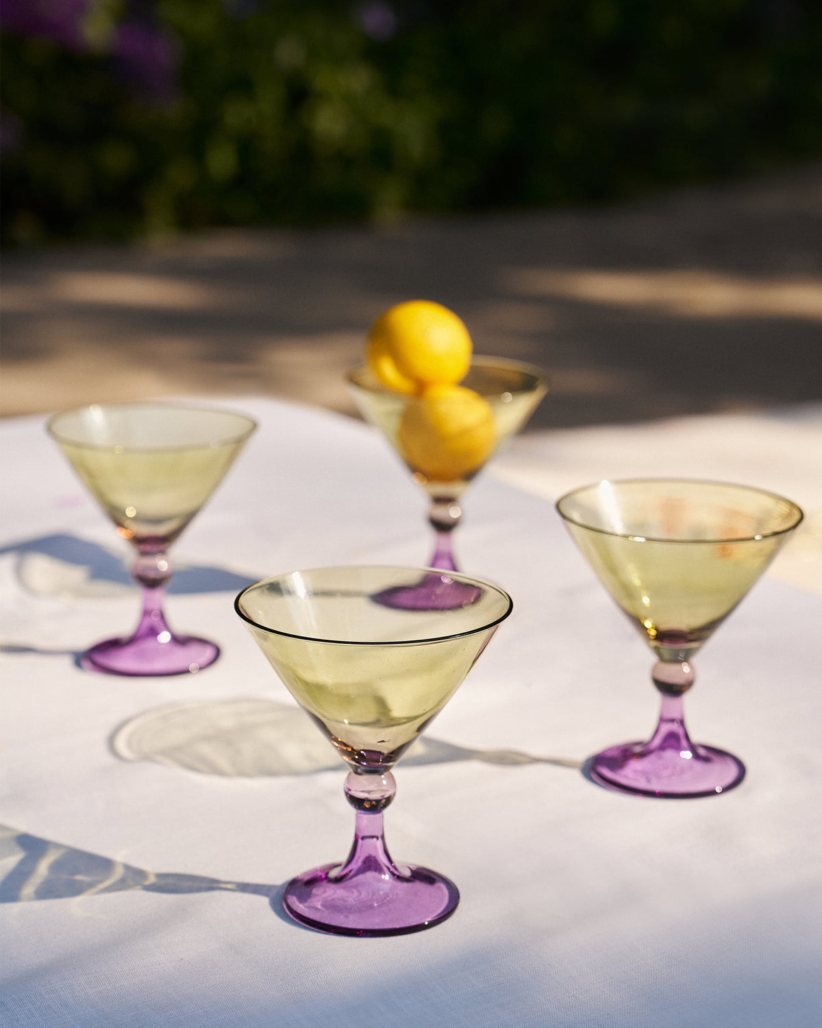 Four Mist cocktail glasses with green bowls and purple stems on a table.