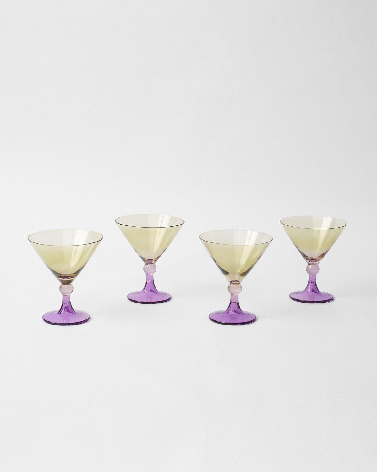 Four Mist cocktail glasses with pale yellow bowls and purple bases.