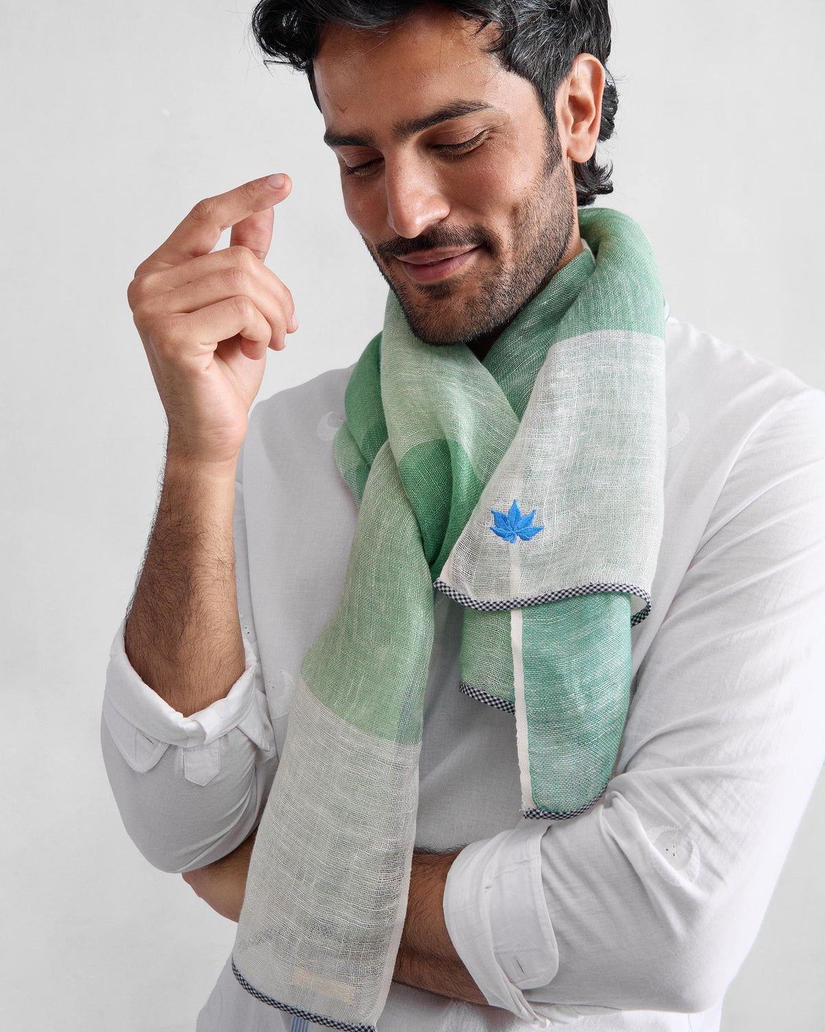 Person wearing a Summer Field Scarf in green and white check with a blue embroidered motif.