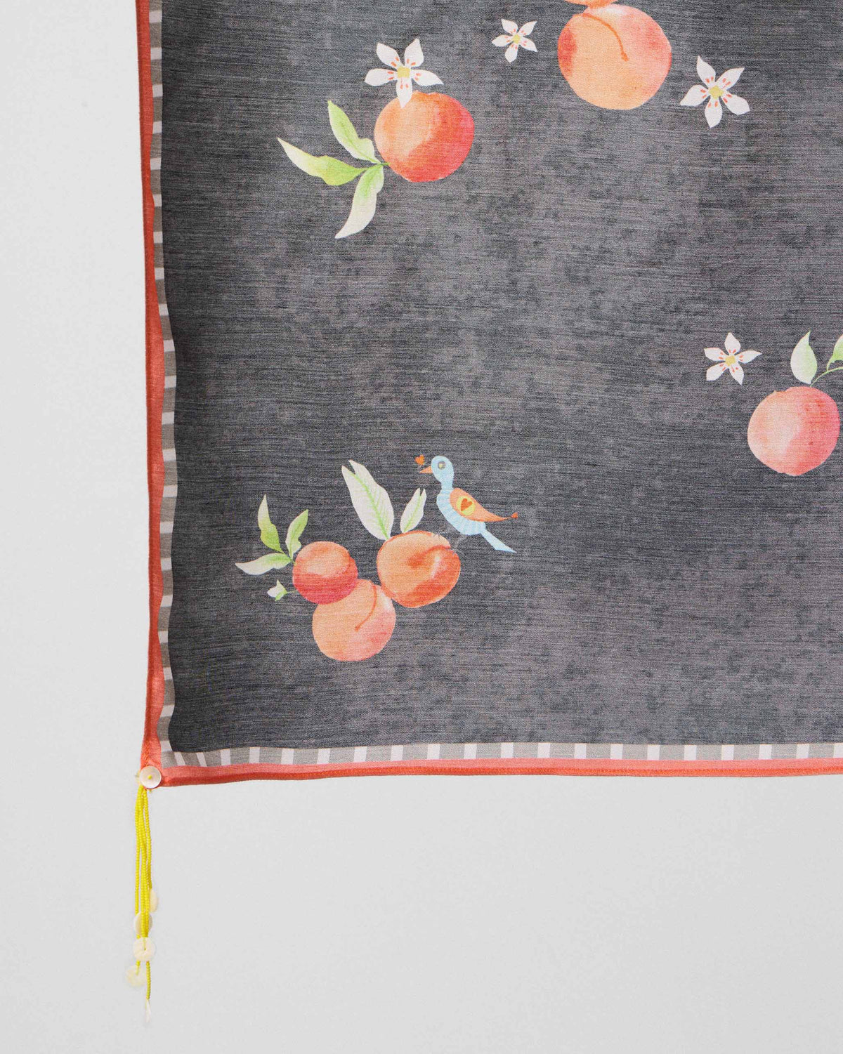 Close-up of peach motifs and a green tassel on a charcoal Apricot Scarf.