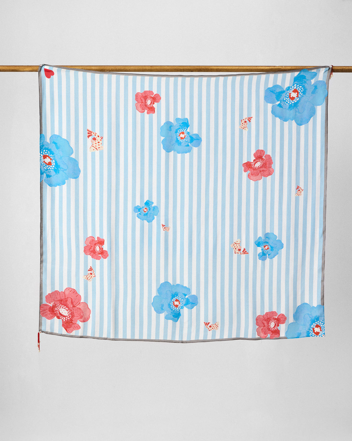 Fields Scarf in ice blue with red and blue flowers, hung from a rod.