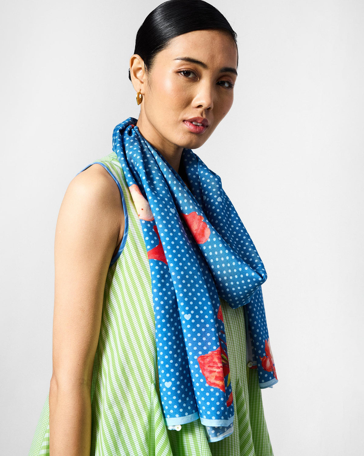 Person wearing the Gulmohar Scarf in blue polka dots with red blossoms, draped at the neck.