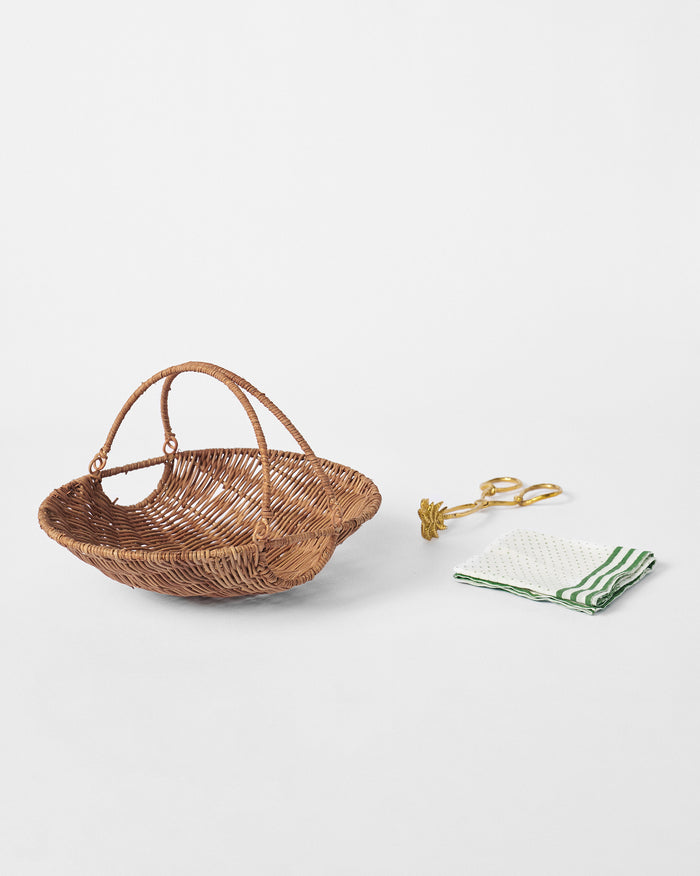 Rattan bread basket set with gold tongs and a green-dotted napkin.