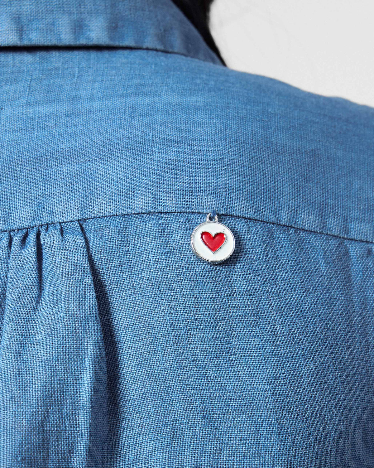 Close-up of a red heart coin hanging from the blue Mati shirt yoke.