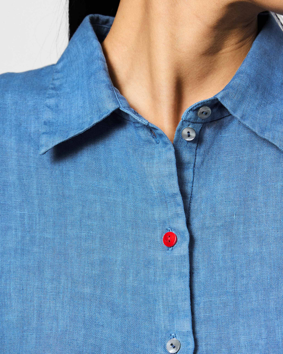 Close-up of a blue Mati shirt collar with a red button on the placket.
