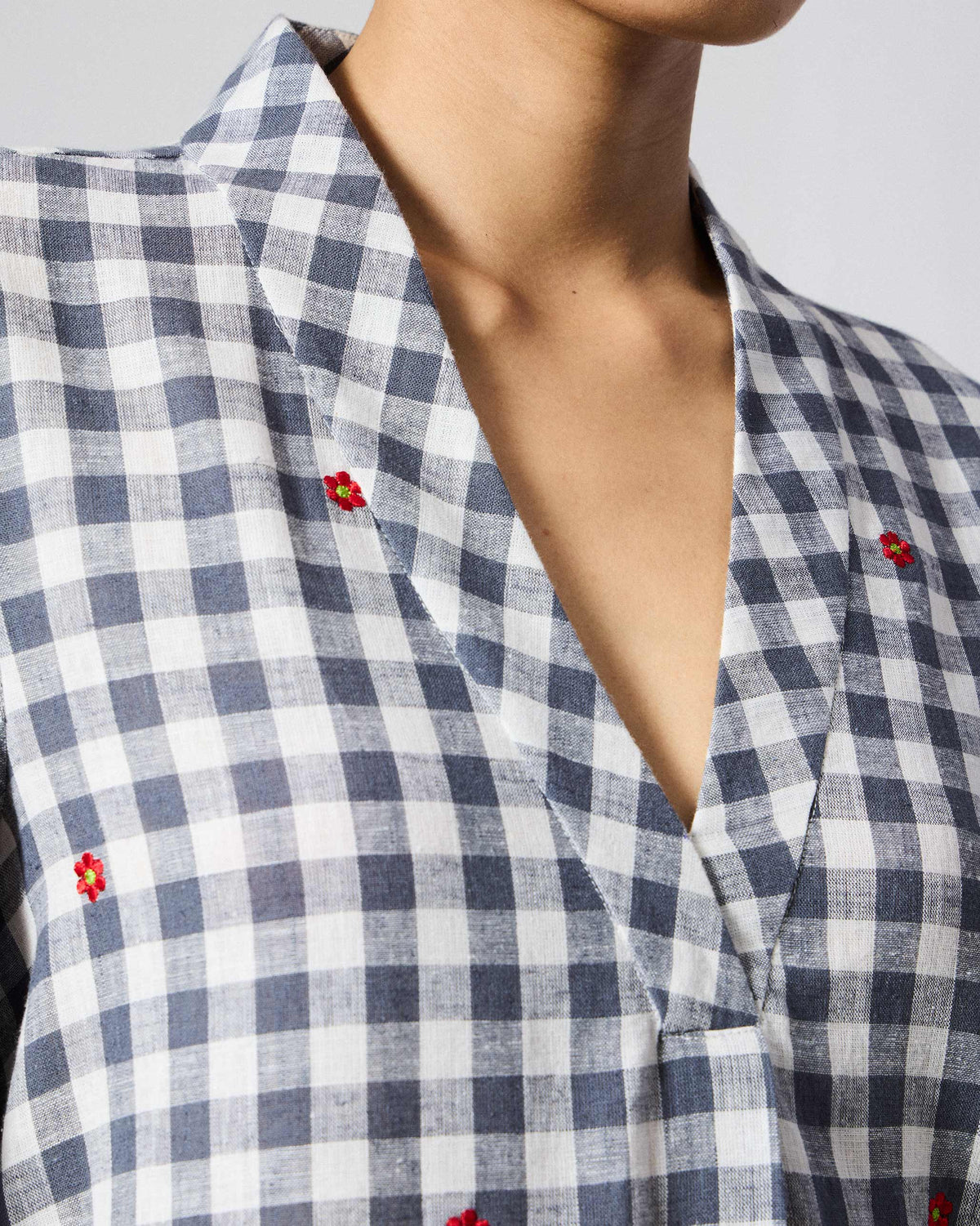 Close-up of a navy check Dhauli Kurta with a V-neck and red flower embroidery.