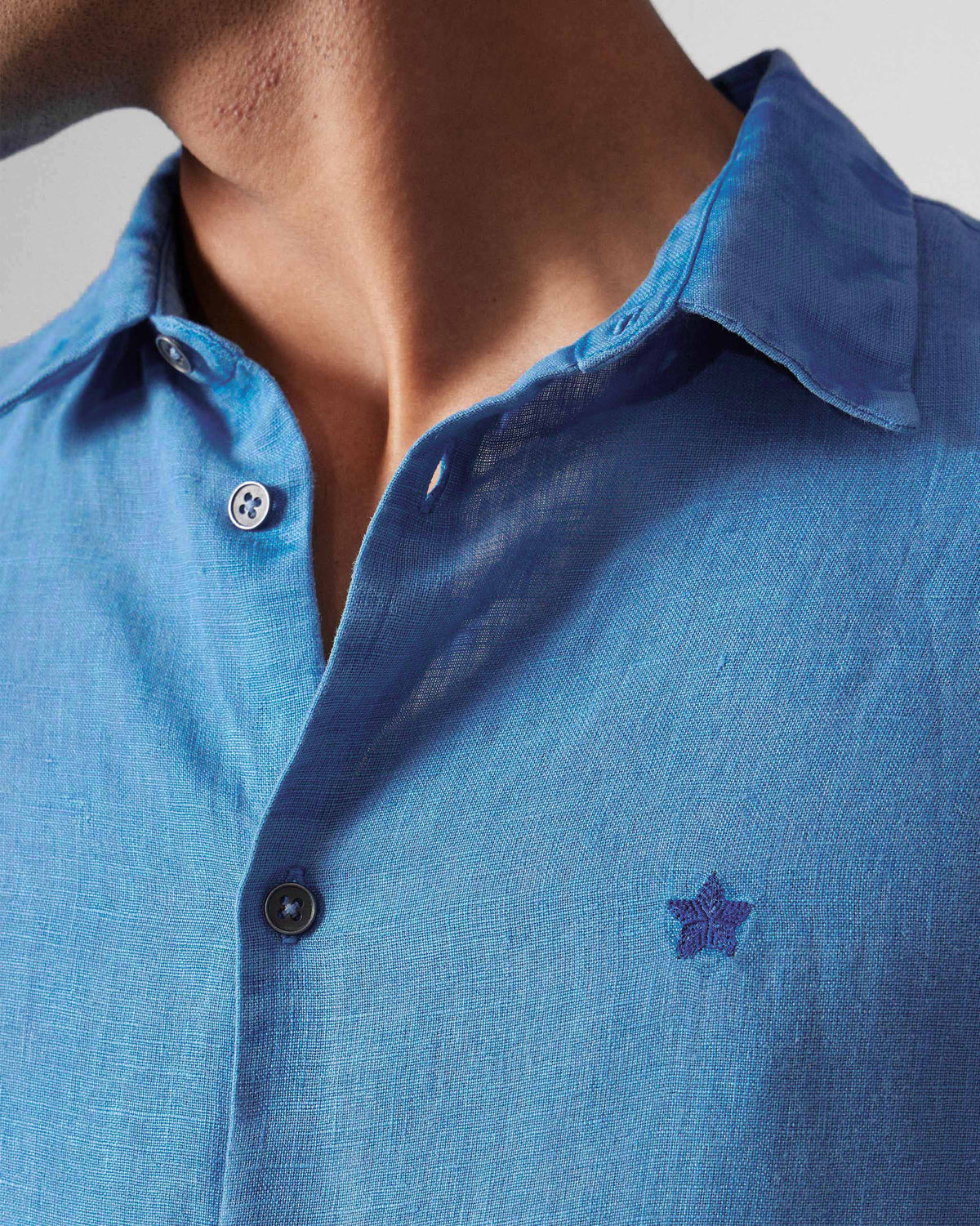 Close-up of a light blue Classic Shirt showing linen texture and a chest star embroidery.