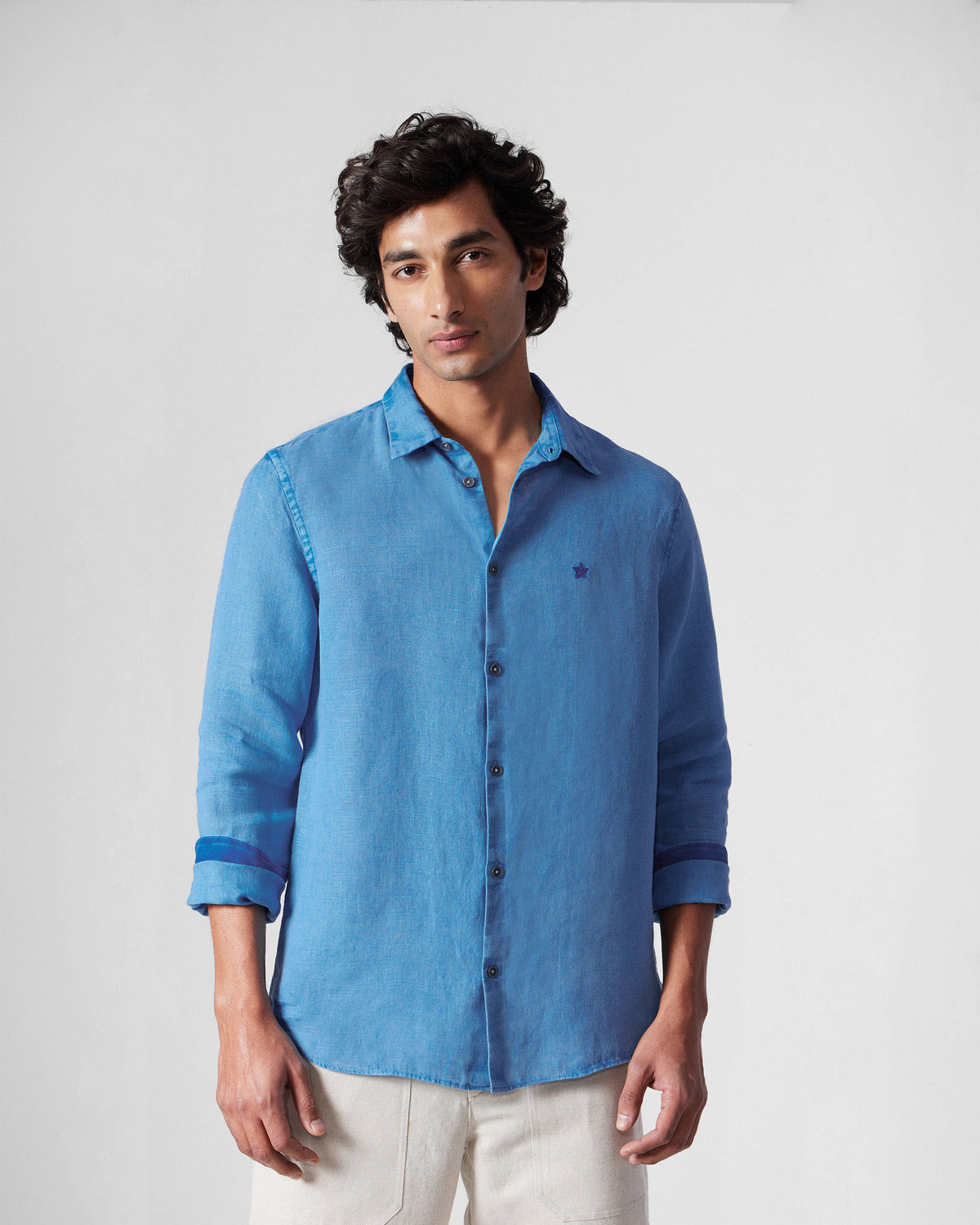Person wearing a light blue Classic Shirt untucked with a chest star embroidery.