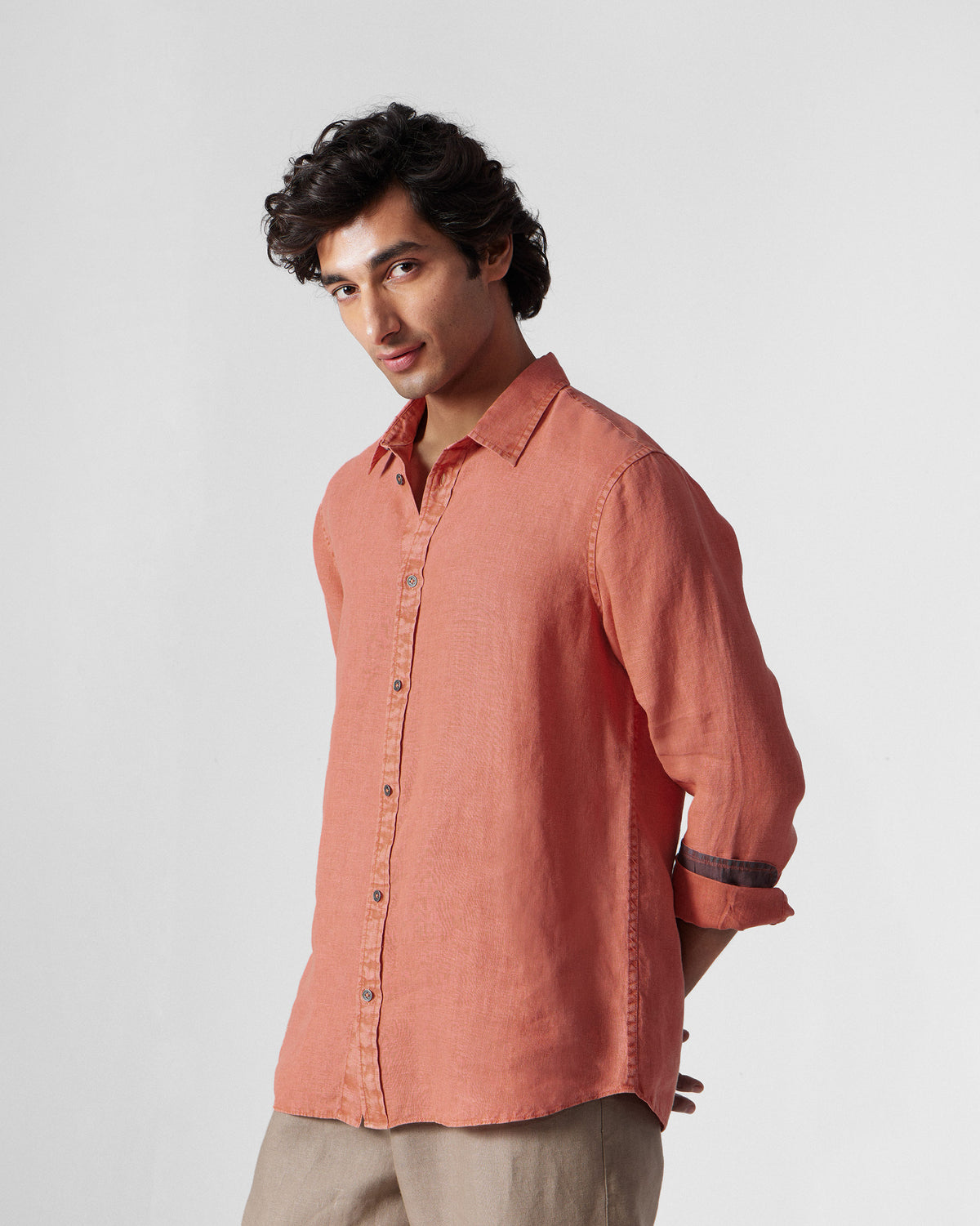 Three-quarter view of a rust Indus Shirt with rolled sleeves and a dark contrast cuff.