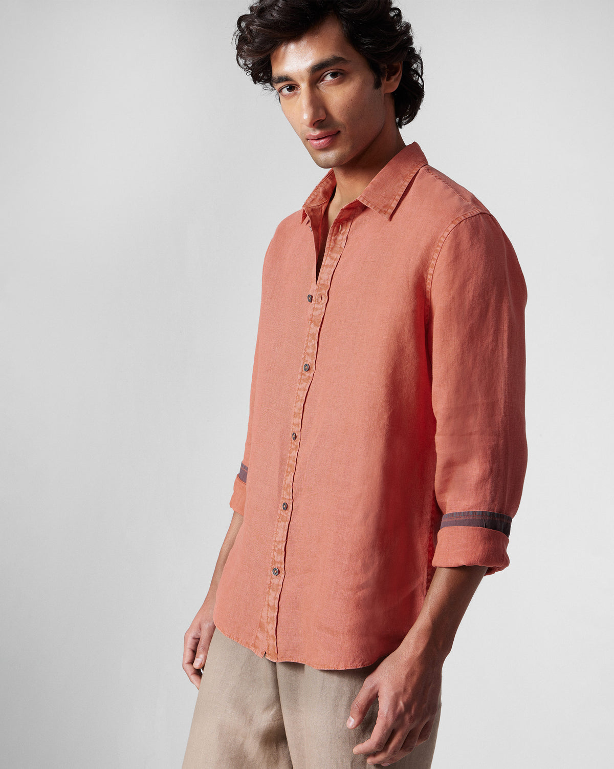 Person wearing a rust Indus Shirt with sleeves rolled to show a dark cuff stripe.