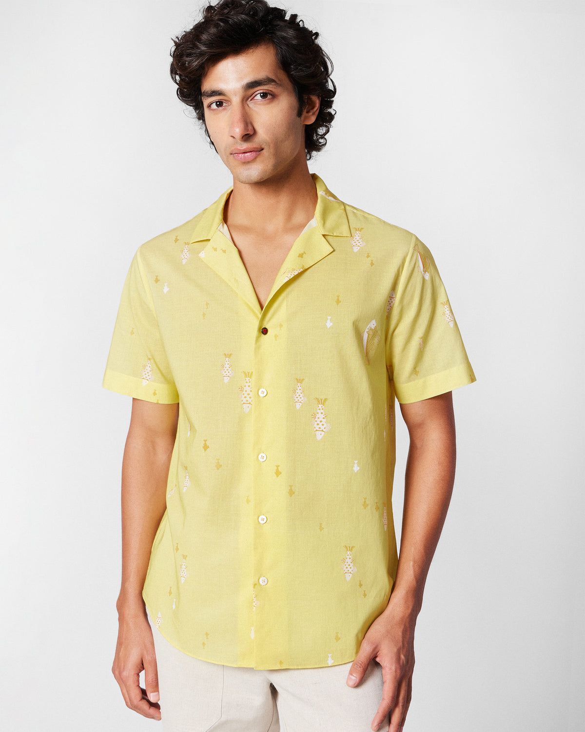 Person wearing a light yellow Mistari Shirt with a white fish print and camp collar.