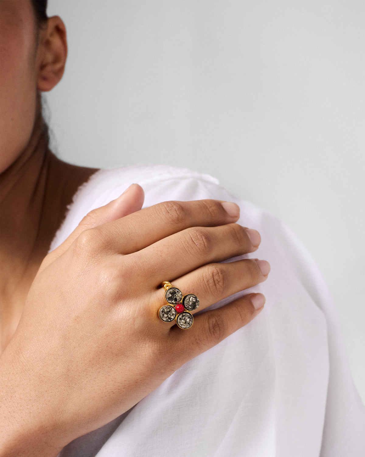 Person wearing a Sindhu gold flower ring with grey stones and a red centre.