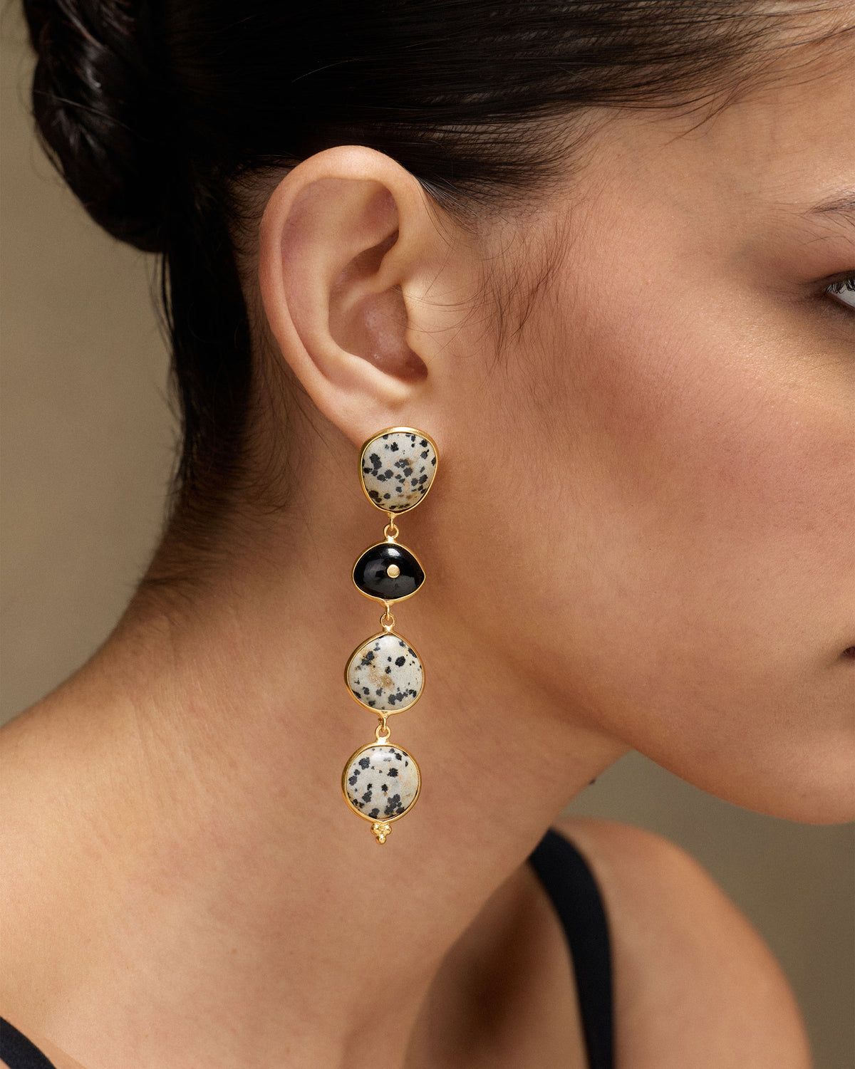Person wearing gold Mountain Danglers with speckled stones and a black stone.