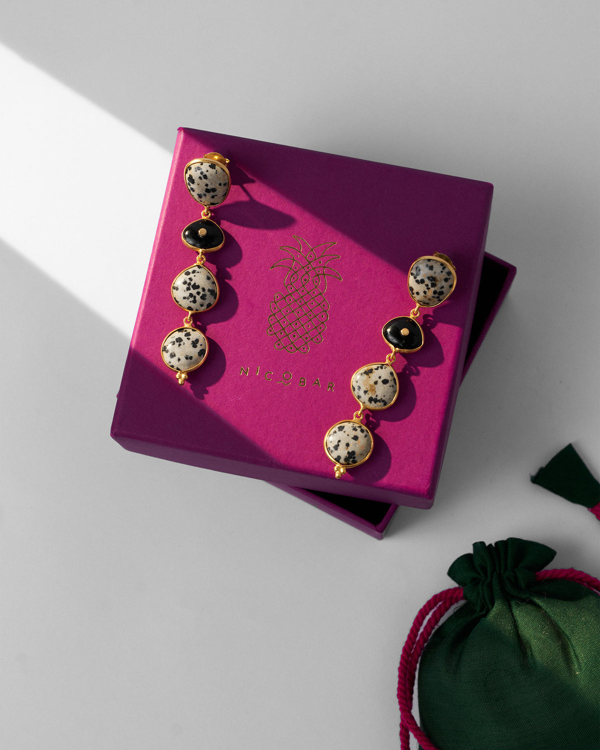 Pair of gold Mountain Danglers on a pink gift box beside a green pouch.